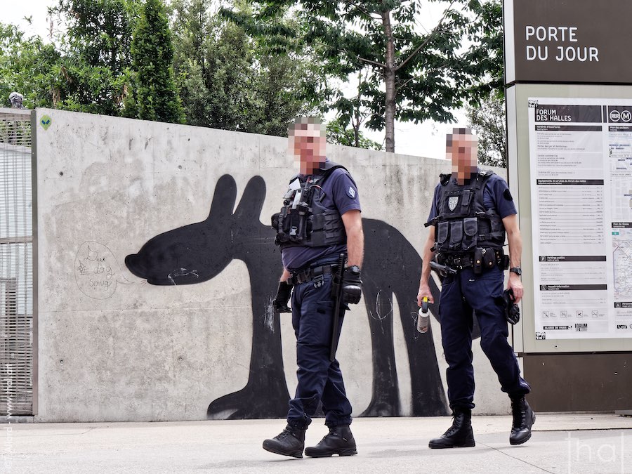 2 policiers armés devant gros chien peint sur un mur